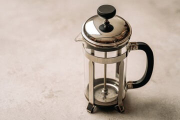 Elegant French press coffee maker on a textured surface with soft lighting and minimalistic background