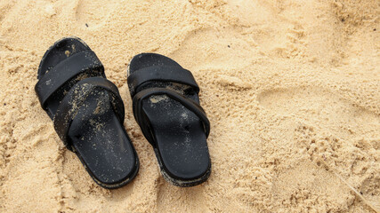 a pair of black sandals scattered with sand on the beach                             