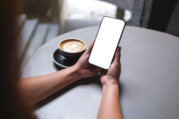 Mockup image of a woman holding and using mobile phone with blank desktop screen in cafe