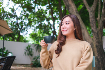 Portrait image of a woman holding and drinking coffee in the outdoors cafe