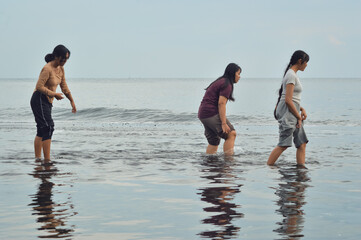 Carefully stepping through the brackish stream, three teenage girls lift their pants as they cross...