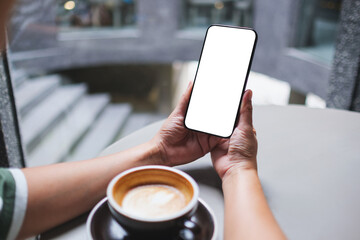 Mockup image of a woman holding and using mobile phone with blank desktop screen in cafe