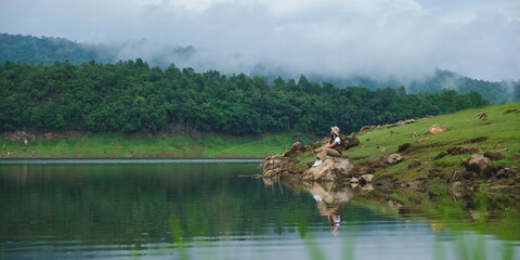A woman sitting by the reservoir and looking at a mountain views on cloudy day
