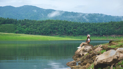 A woman sitting by the reservoir and looking at a mountain views on cloudy day