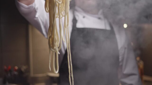 Close-up view of hands of chef stirs the pasta in the pan with boiling water. Preparing Asian udon noodles in a saucepan.