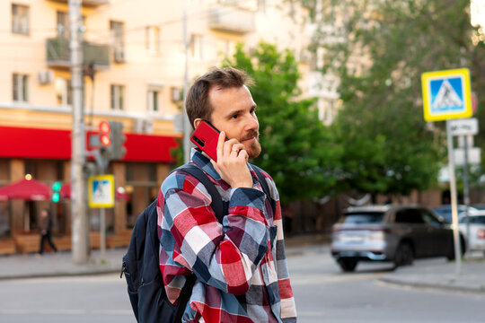 Young man with backpack having phone call on street. Guy with beard talking on smartphone outdoors. Concept of digital communication, connection and casual lifestyle