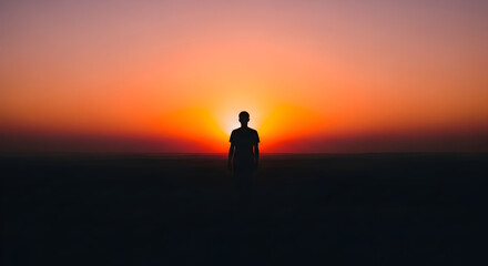 Fototapeta premium Silhouette of a person standing alone during a vibrant sunset with colorful sky and horizon creating a peaceful and contemplative mood perfect for nature and reflection themes