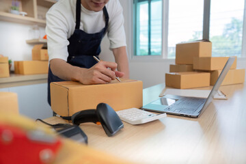 Efficient Packaging. Young man labeling boxes while using laptop in home office.