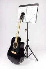 black guitar with a music stand and a music notebook on a white background. an isolated object. close-up.