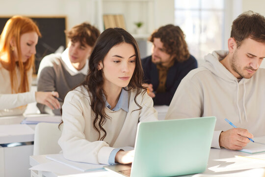 Students group working and study at laptop online at desk in college class, trainee interns sitting watching webinar on computer screen writing, focused studying online, young people learning language