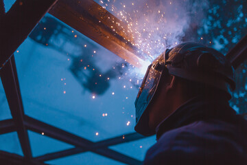 Welder working with protective helmet and sparks in dark workshop
