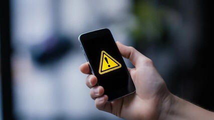 Hand holding smartphone displaying a caution warning sign on its screen - Powered by Adobe