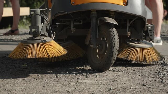 Round coarse brushes on street cleaning tricycle, close-up. Modern electric cleaning equipment in city park. Caring for cleanliness of urban environment.