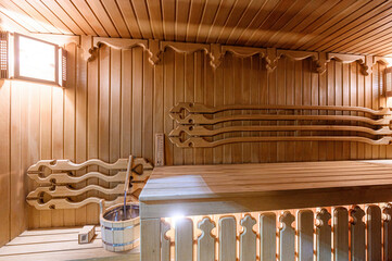 Warm sauna interior with wooden benches, walls, and a water bucket. Cozy and inviting ambiance