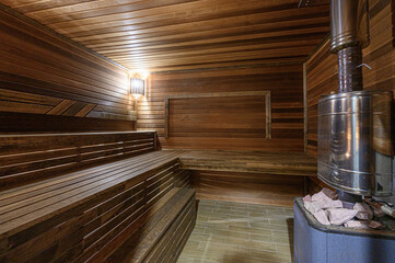 warm-toned sauna interior featuring wooden benches, walls, and ceiling. A metallic stove with...