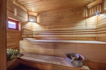 wooden sauna interior with benches, a wash basin, and a birch whisk. Soft light
