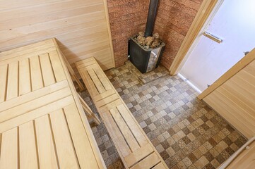 sauna interior featuring wooden benches, tiled floor, and a stove with stones. The walls are clad...