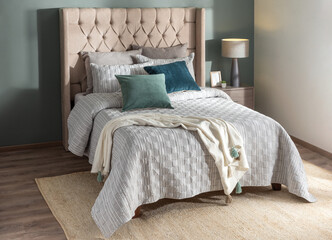 Front view of a transitional style bedroom designed for relaxation, with a tall beige tufted headboard, layered gray and white bedding, velvet pillows and soft daylight enhancing a peaceful atmosphere