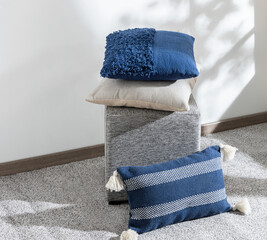 Stacked textured and woven throw pillows in navy blue and beige on a modern grey ottoman, placed on...