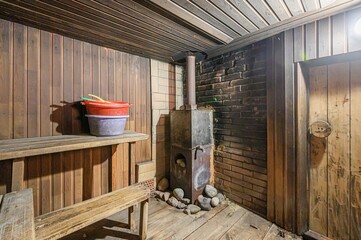 Rustic sauna interior with wooden benches, a metal stove, and brick walls. Buckets sit on a bench,...