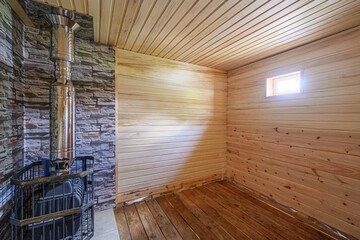 cozy sauna interior with wood paneling, a stone accent wall, and a metal stove. Warm lighting