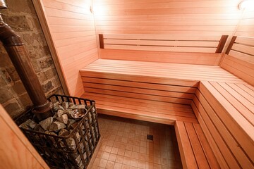 Cozy sauna interior features wooden benches, stone-filled heater, and tiled floor. Warm lighting...
