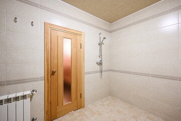 bright bathroom with beige tiles and a wooden door with a frosted glass panel. A shower is visible...