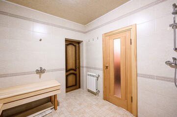 Tiled sauna interior. Features wooden bench, two doors, shower, and radiator. Neutral tones and clean design