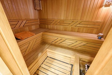 cozy sauna interior with wooden benches, walls, and floor. Towel, bucket, and heater are visible....
