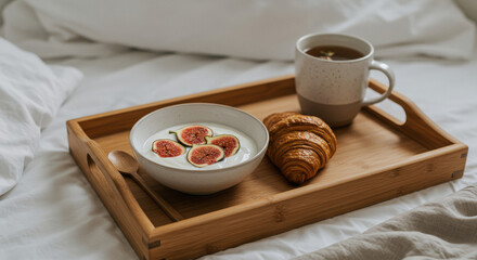 Enjoying a minimalistic breakfast in bed with yogurt, figs, croissant, and tea