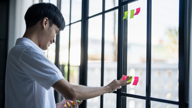 Man organizing project tasks Colorful sticky notes on glass of meeting room
