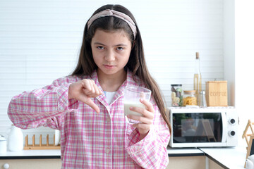Cute teenage girl doesn't like to drink milk and makes a thumbs-down gesture.