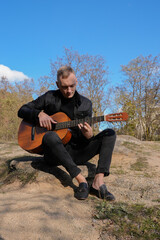 Blonde man playing string guitar outdoors in autumn forest. Concept of sound therapy, mental health...