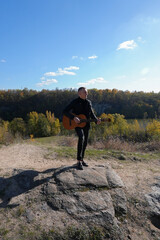 Blonde man playing string guitar outdoors in autumn forest. Concept of sound therapy, mental health...