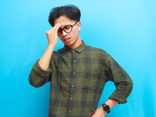 Tired young Asian man in casual shirt suffering from headache or migraine, stressed Asian man...