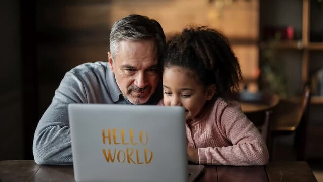 A man and a young girl intently focus on a laptop screen displaying "Hello World," suggesting a learning or coding experience.