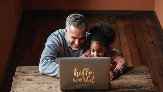 A smiling father and daughter lean over a laptop, sharing a moment of learning and discovery as the screen displays "hello world" in a golden script.