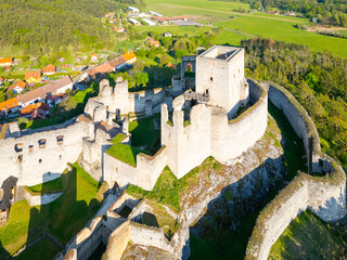 An aerial view captures the ancient ruins of Rabi Castle, showcasing its impressive stone walls and surrounding landscape in Czechia. The castle sits atop a hill, surrounded by lush greenery.