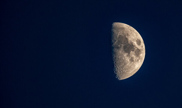 First quarter moon glowing in a dark night sky. Sharp details of lunar craters and surface texture. Minimalist astronomical photography of the moon against a deep black background. nasa