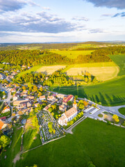 Bohutin Town is captured from above, showcasing its charming layout. Green fields stretch into the distance, complemented by a historic church and a cemetery. The sun casts long shadows.