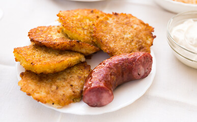 Fried grated potato pancakes with fried sausage on white plate