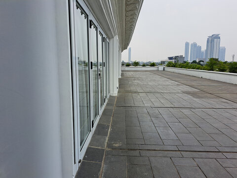 A modern white wall exterior with glass doors and a spacious tiled terrace, overlooking city skyscrapers in the distance on a clear day