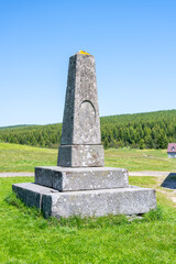 A stone pyramid stands proudly in Jizerka Village, surrounded by lush green mountains and blue skies. It is a notable landmark in the Czech Republic, attracting visitors all year round.
