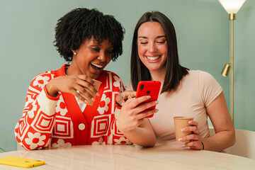 Two cheerful females excitedly gathered together, captivated by a smartphone as they watch an...
