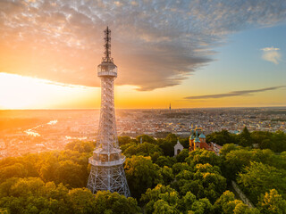 The Petrin Lookout Tower emerges against a vibrant sunrise in Prague, illuminating the skyline. This iconic structure is surrounded by lush greenery, offering a stunning view of the city.
