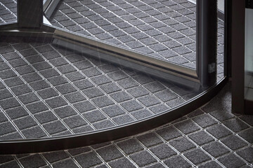 Revolving glass door with modern grid-patterned gray flooring in a contemporary commercial space.