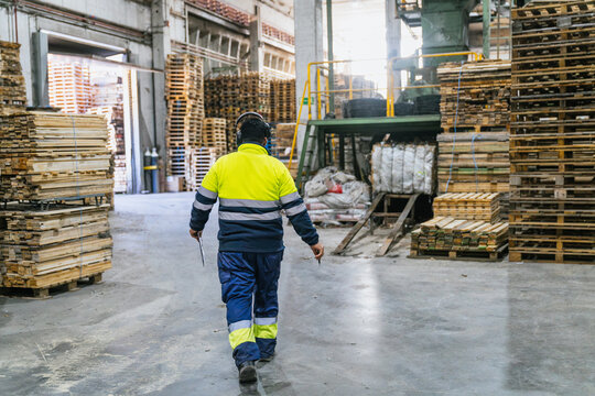 Supervisor wearing safety equipment walking through a wooden pallet recycling factory, checking on production and safety procedures