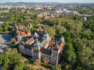 Obraz premium Morning drone photo over Budapest’s City Park showing Vajdahunyad Castle in foreground, with BalloonFly, Széchenyi Thermal Bath, and the Biodóm in one wide scenic aerial frame. 