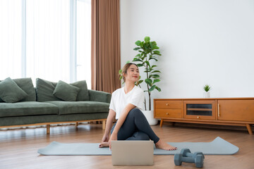 Young Asian woman stretching yoga workout on exercise mat while online training class with computer...