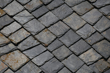 Stone tiles on roof of an old house. Grey and black squares with natural stone texture. Vintage roof